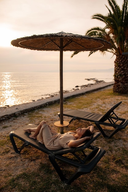 Vue d'angle élevé d'une femme insouciante allongée sur une chaise de pont noire sous un parapluie de paille près d'un palmier au bord de la mer Touriste féminine gardant les yeux fermés et profitant des vacances d'été en Croatie