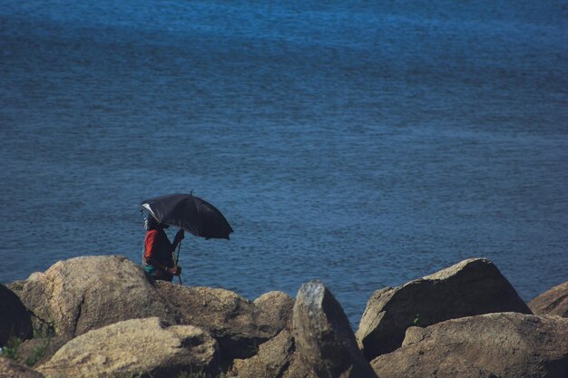 Photo vue d'angle élevé d'une femme avec un parapluie debout sur une plage rocheuse