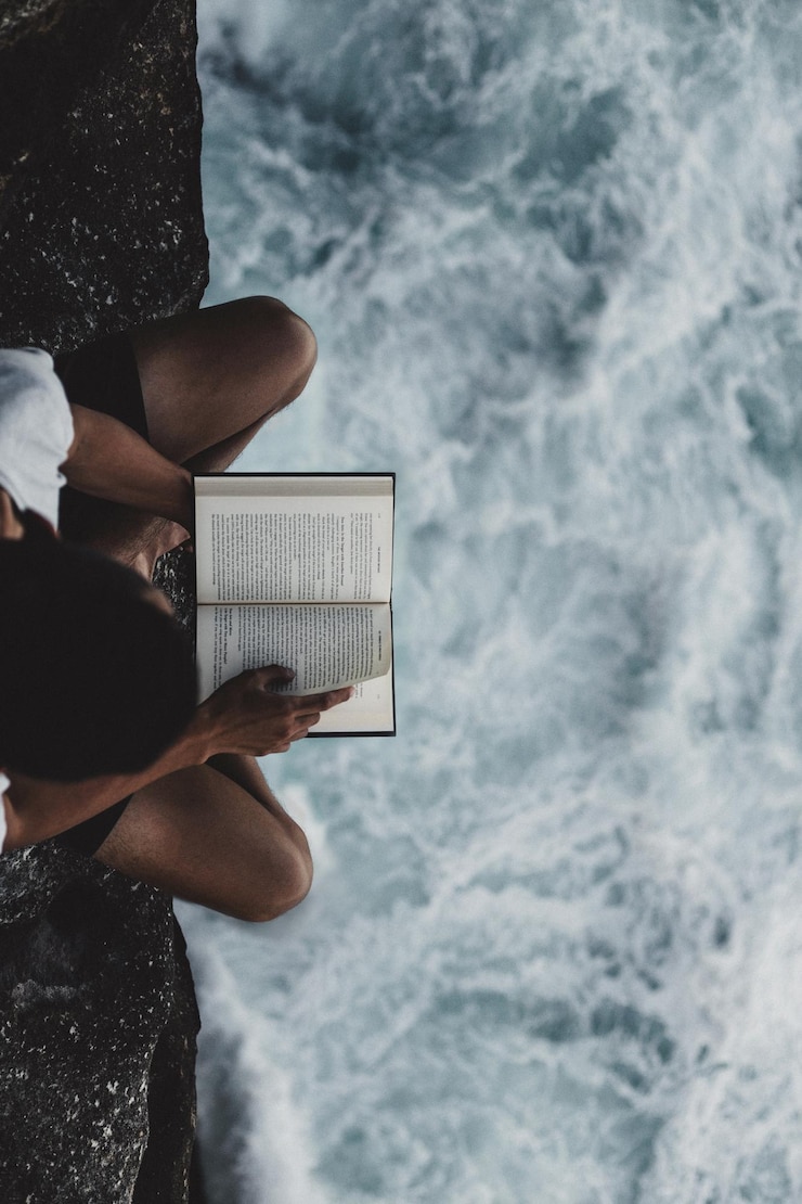 Photo vue d'angle élevé d'un homme lisant un livre sur la formation rocheuse en mer