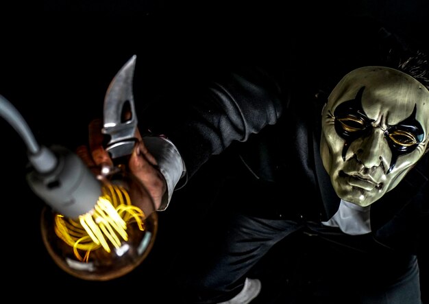 Photo vue d'angle élevé d'un homme portant un masque tenant une ampoule éclairée contre un fond noir