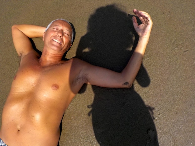 Vue d'angle élevé d'un homme sans chemise allongé sur le sable par l'ombre d'une femme sur la plage