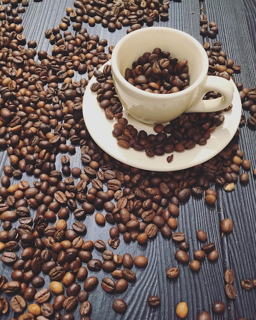 Vue d'angle élevé de la tasse et de la soucoupe avec des grains de café torréfiés sur la table