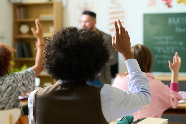 Photo vue arrière d'un adolescent levant la main pour répondre à la question de l'enseignant