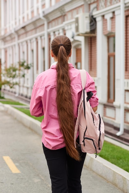 Vue arrière de l'adolescente en chemise rose avec sac à dos à l'extérieur