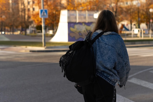Vue arrière d'une adolescente méconnaissable avec sac à dos marchant dans la rue Une jeune femme marche dans la rue de la ville sac à dos noir sur le dos