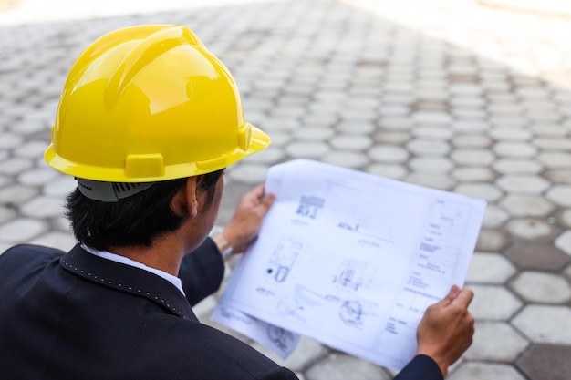 Vue arrière architecte constructeur avec casque jaune étudiant le plan d'aménagement des chambres