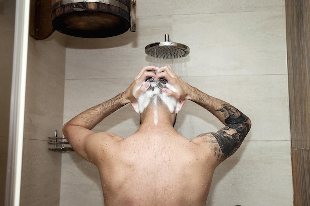 Vue arrière beau jeune homme prenant une douche shampooing tête de lavage debout sous l'eau qui tombe dans les bains publics