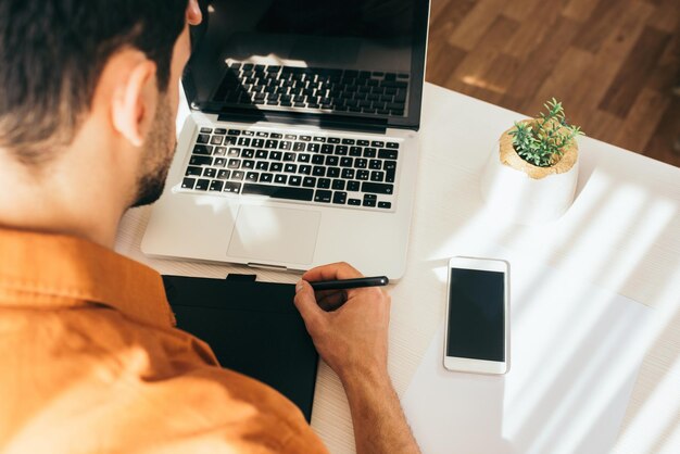 Vue arrière d'un bel homme dans les tons tapant sur un ordinateur portable avec un écran vierge bénéficiant d'une communication en ligne Processus de travail avec un stylo numérique Mise au point sélective Concept d'entreprise et de technologie