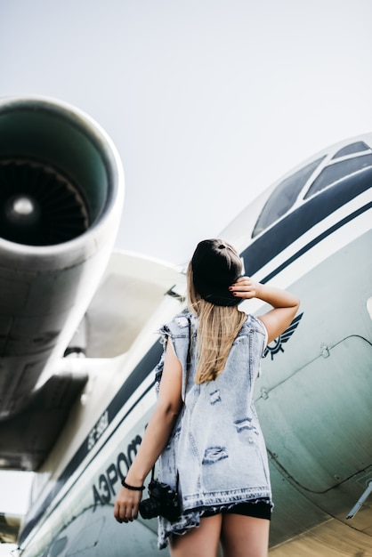 Vue arrière de la belle femme touristique avec un vieux caméra vintage de film posant près de l&#39;avion