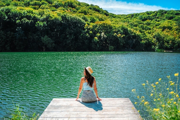 Vue arrière Une belle jeune femme est assise sur une jetée en bois sur un charmant lac de montagne azur