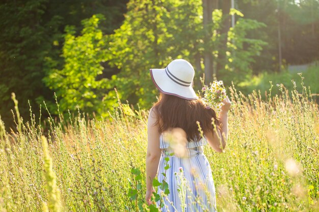 Vue arrière de la belle jeune femme marchant parmi les fleurs sauvages aux beaux jours d'été. Concept de la joie de communiquer avec la nature estivale