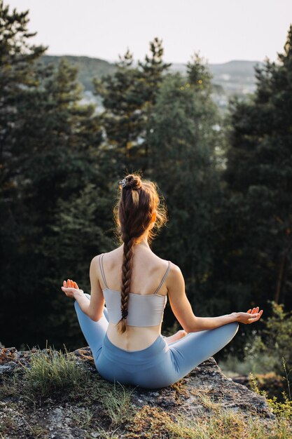 Photo vue arrière belle jeune femme pratiquant le yoga sur le rocher en plein air dans la forêt d'été