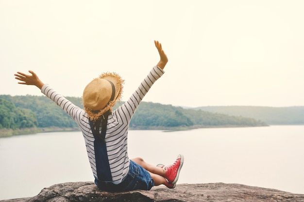 Vue arrière complète de la femme avec les bras levés assise au bord du lac contre un ciel clair