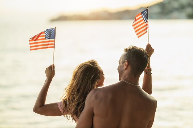 Vue arrière d'un couple aimant avec drapeau national américain profitant d'une journée de détente sur la plage.