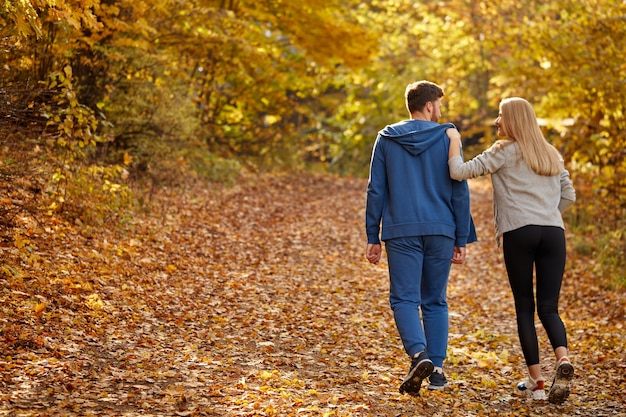 Vue arrière sur couple appréciant le jogging sur une route de campagne à travers la belle forêt d'automne, exercice