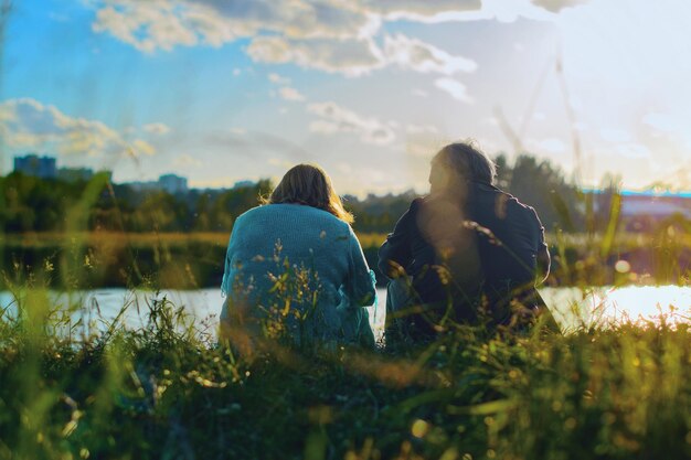 Photo vue arrière d'un couple assis au bord du lac contre le ciel