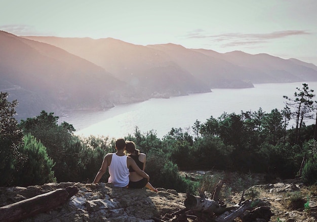 Photo vue arrière d'un couple assis sur un rocher contre le ciel