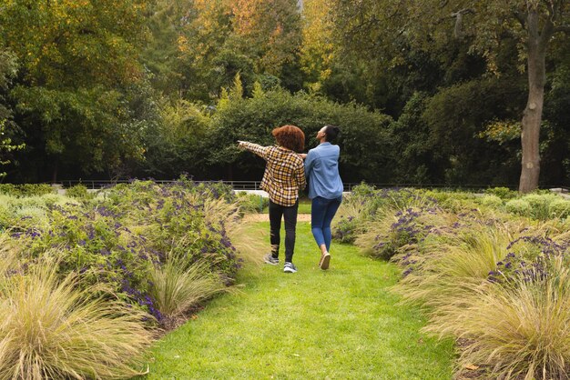 Photo vue arrière d'un couple heureux et diversifié se tenant par la main marchant dans le jardin et pointant