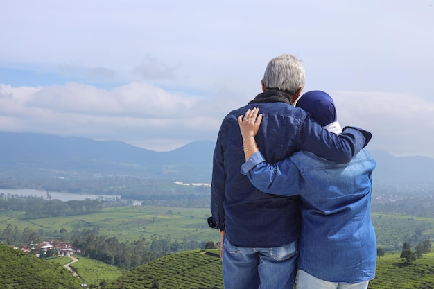 Vue arrière d'un couple de personnes âgées romantiques asiatiques regardant une plantation de thé et un lac de paysage spectaculaire