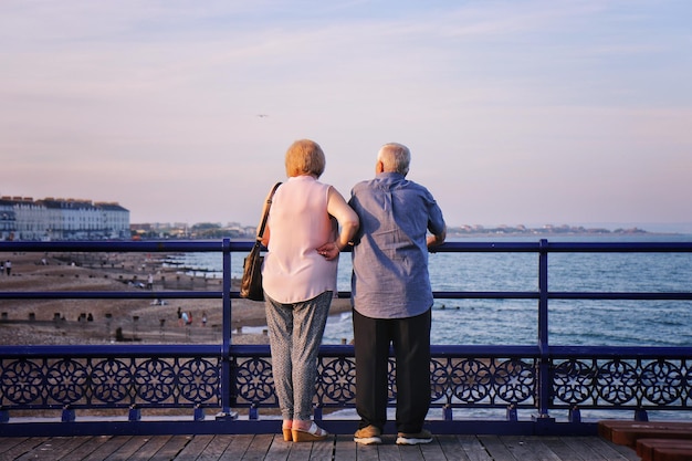 Vue arrière d'un couple regardant la mer alors qu'ils se tiennent par un garde-corps contre le ciel au coucher du soleil
