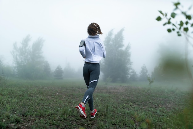 Vue arrière de la coureuse faisant du jogging dans la nature le matin brumeux Espace de copie