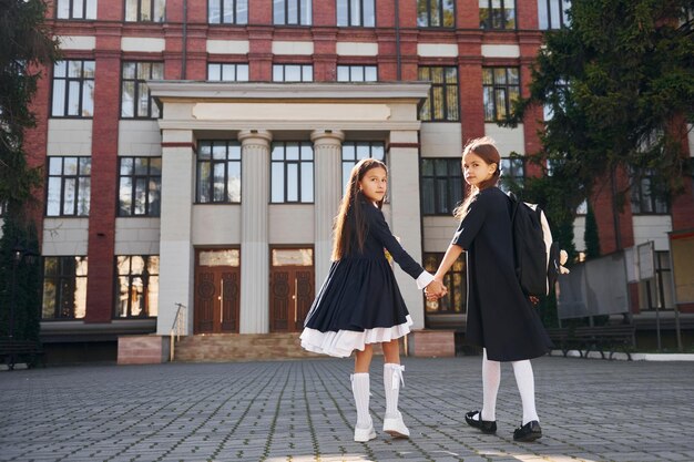 Vue arrière Deux écolières sont à l'extérieur ensemble près du bâtiment de l'école