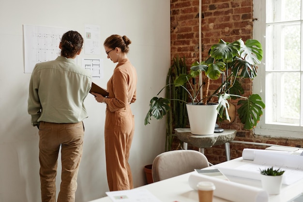 Vue arrière de deux jeunes créatifs planifiant un projet de conception par mur en studio, espace de copie