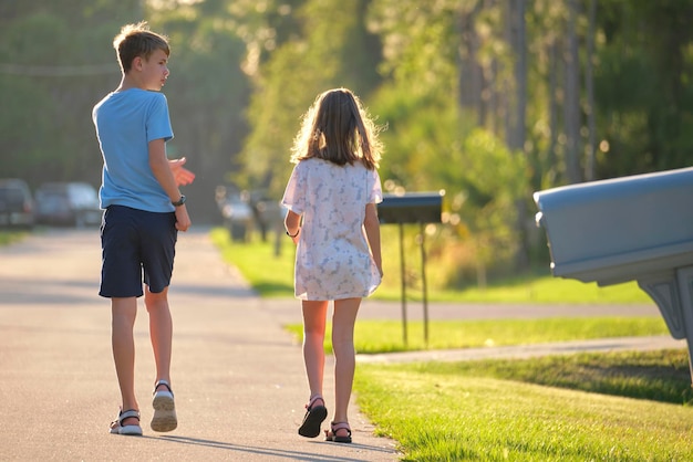 Vue arrière de deux jeunes enfants adolescents fille et garçon frère et sœur marchant ensemble dans une rue de banlieue par une belle soirée ensoleillée