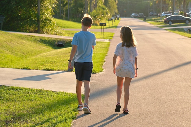 Vue arrière de deux jeunes enfants adolescents fille et garçon frère et sœur marchant ensemble dans une rue de banlieue par une belle soirée ensoleillée