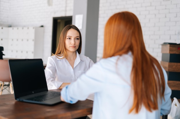 Vue arrière de deux jeunes femmes d'affaires sérieuses et concentrées discutant de nouveaux projets partageant des idées assises au bureau l'une en face de l'autre dans la salle de réunion du bureau. Concept de ressources humaines d'entretien d'embauche.