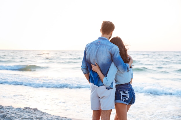 Vue arrière du beau jeune couple debout et s'embrassant sur la plage