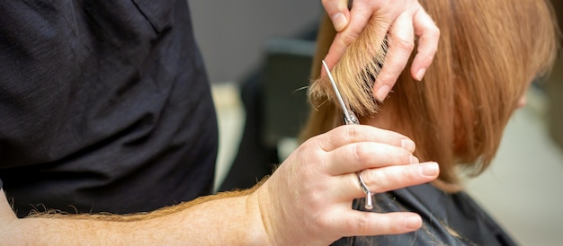 Photo vue arrière du coiffeur coupe les cheveux rouges ou bruns à la jeune femme dans un salon de beauté. coupe de cheveux dans un salon de coiffure. flou artistique