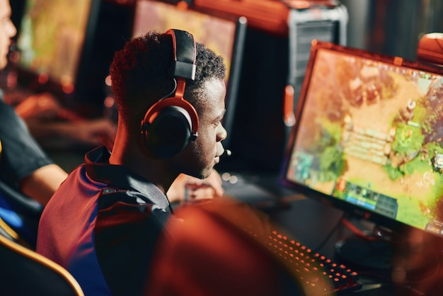 Vue arrière du concept Cybersport d'un joueur professionnel de type africain concentré portant des écouteurs à la recherche