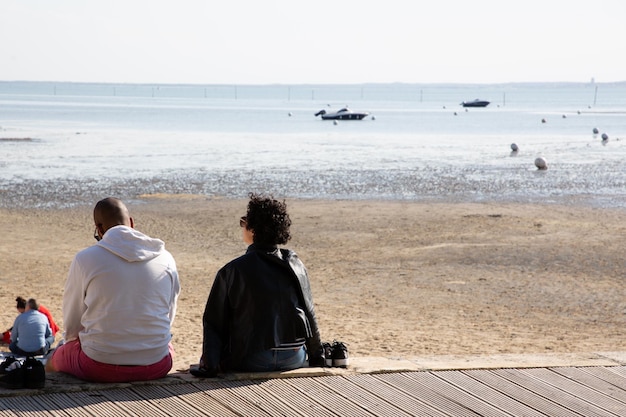 Vue arrière du couple assis sur une plage en bois au bord de la mer