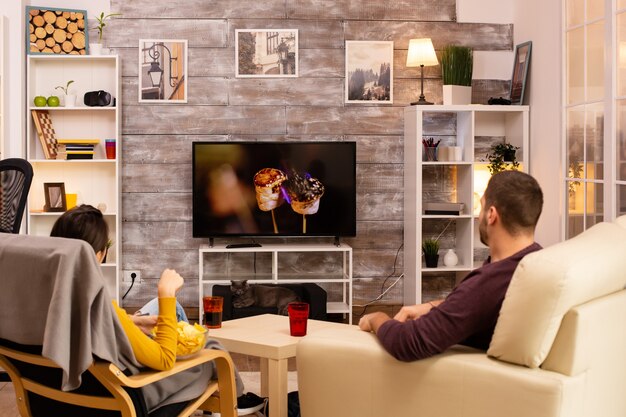 Vue arrière du couple dans le salon regardant un film à la télévision tout en mangeant des plats à emporter