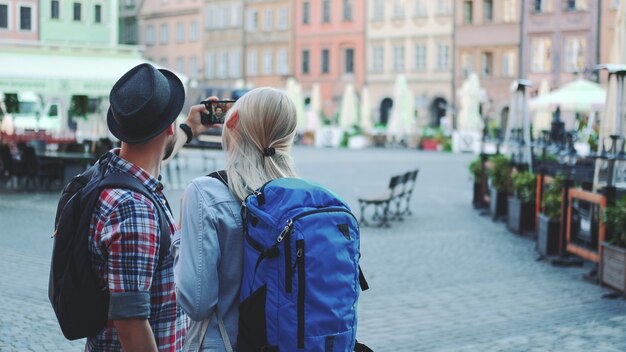 Vue arrière du couple de jeunes touristes faisant selfie sur smartphone dans le centre-ville