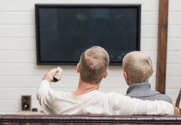 Vue arrière du couple de personnes âgées regardant quelque chose à la télévision