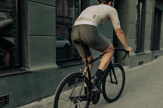 Vue arrière du cycliste caucasien musclé en vêtements de sport et casque de sécurité faisant du vélo le long de la rue de la ville Concept de personnes sport et activité de plein air