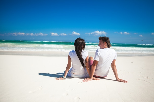 Vue arrière du jeune couple amoureux assis sur une plage tropicale blanche