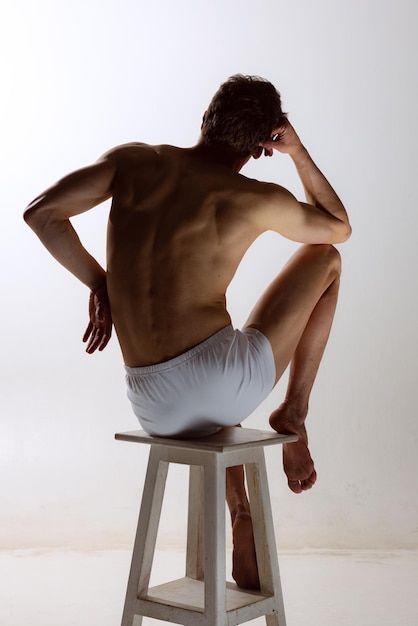 Vue arrière du jeune homme musclé torse nu portant des boxeurs blancs debout isolé sur fond gris