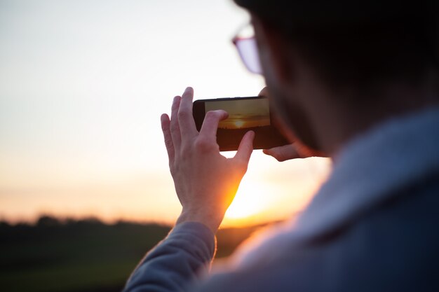 Vue arrière du jeune homme prendre des photos du coucher du soleil par smartphone