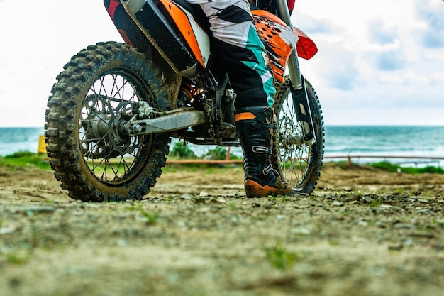 Vue arrière du jeune homme regardant au loin et assis sur une moto sur la plage au coucher du soleil