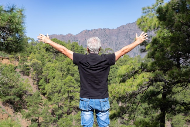 Vue arrière du Senior Man Enjoying Trekking Day on Mountain Standing with Open Arms Admiring Nature