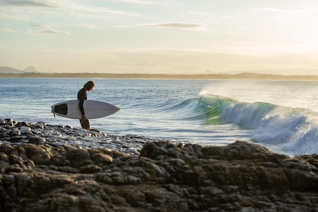 Vue arrière du surfeur marchant sur des rochers avant de sauter dans l'eau Espace de copie Concept de sport aquatique