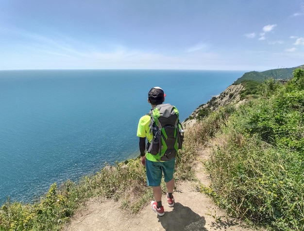 Vue arrière du touriste avec sac à dos debout au bord de la falaise et regardant la mer