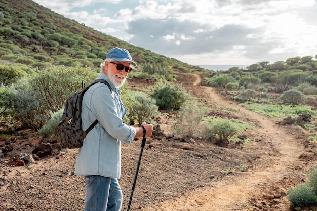 Vue arrière du vieil homme senior appréciant le trekking dans la campagne le long de la mer Homme de race blanche âgé avec chapeau et sac à dos marchant dans le sentier