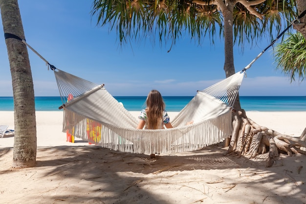 Vue arrière du voyage femme assise sur un hamac blanc sur la plage de sable