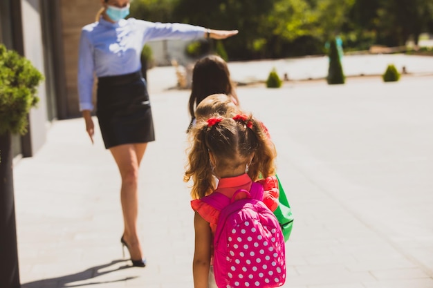 Vue arrière des écoliers se tiennent les uns derrière les autres près de l'école L'enseignant montre comment déterminer la distance sociale pendant une épidémie