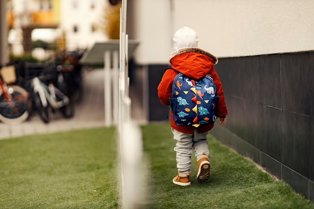 Vue arrière d'un enfant de la maternelle avec un cartable sur le dos marchant à l'extérieur