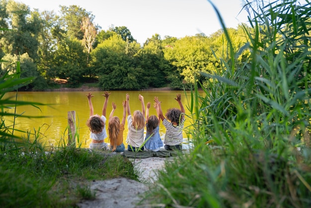 Photo vue arrière des enfants heureux assis au bord du lac